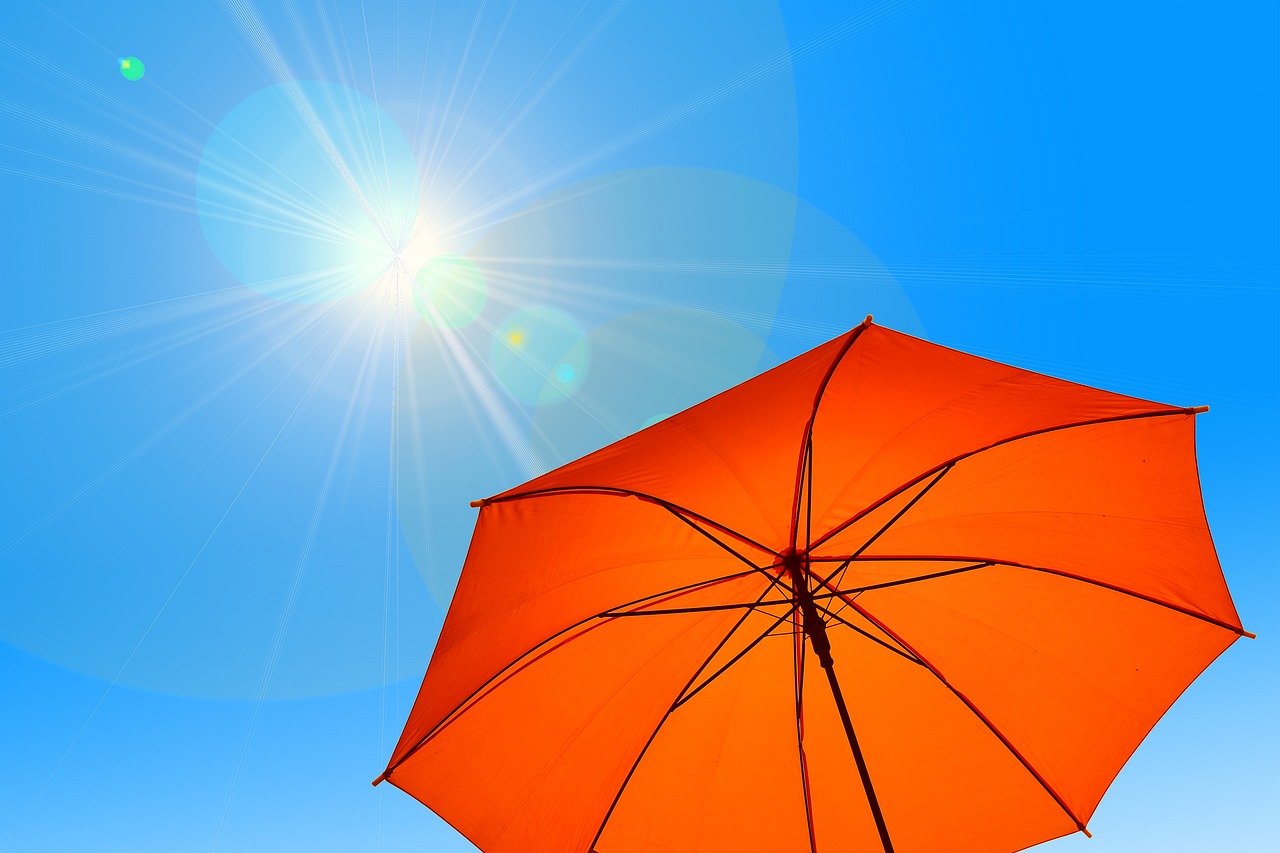 Orangefrabener Regenschirm wird als Schutz in das gleißendes Sonnenlicht gehalten.