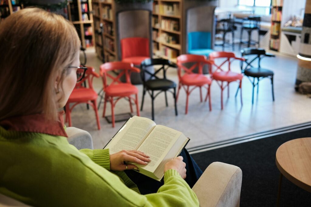 Frau sitzt in Bücherei und liest ein Buch